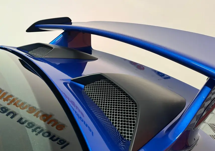 Gros plan sur l’aileron arrière bleu saphir de la Porsche 911 GT3 avec prises d’air noires et grille métallique.
