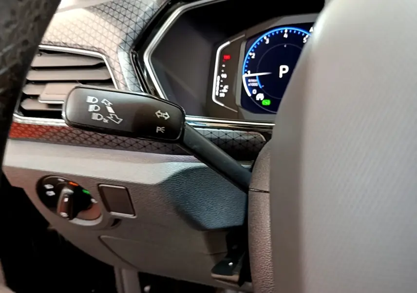 Détail du commodo gauche et tableau de bord numérique bleu du Volkswagen T-Cross 1.0 TSI noir, vue intérieure côté conducteur.