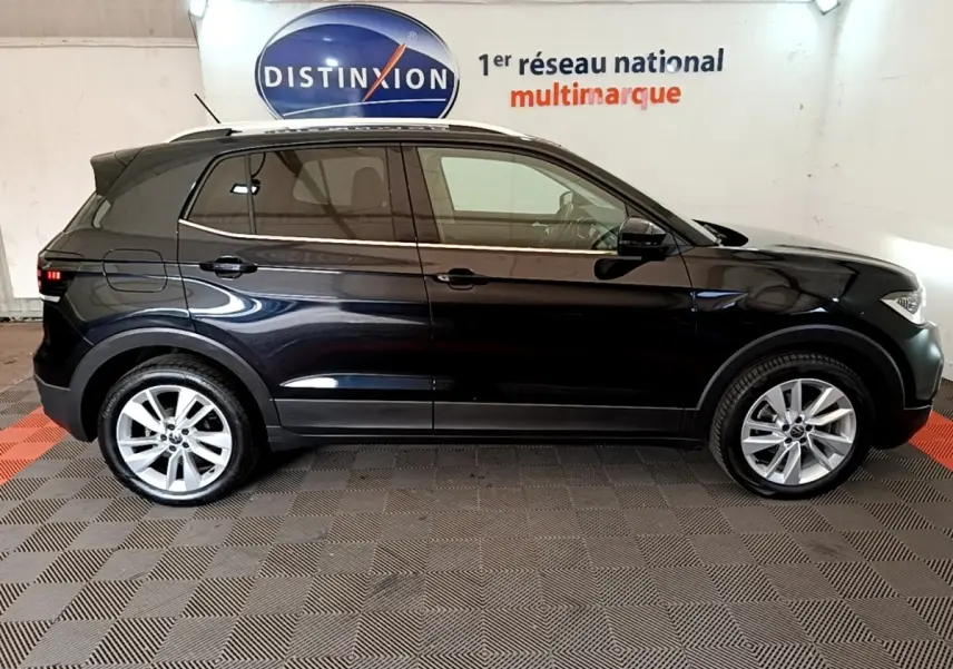 Profil droit d’un Volkswagen T-Cross noir 2022, avec jantes alliage et vitres teintées, sur fond intérieur showroom.