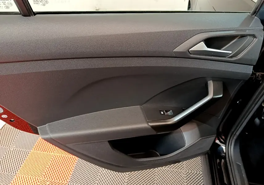 Vue rapprochée de la porte avant gauche noire du Volkswagen T-Cross 2022, avec poignée et commande de vitre électrique.