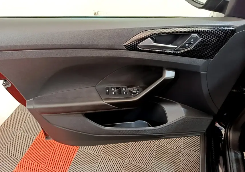 Vue intérieure du panneau de porte avant gauche noir du Volkswagen T-Cross avec commandes électriques et poignée design texturée.