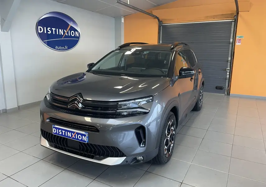 Vue 3/4 avant d'un Citroën C5 Aircross hybride gris platinium avec jantes biton et toit noir en showroom.