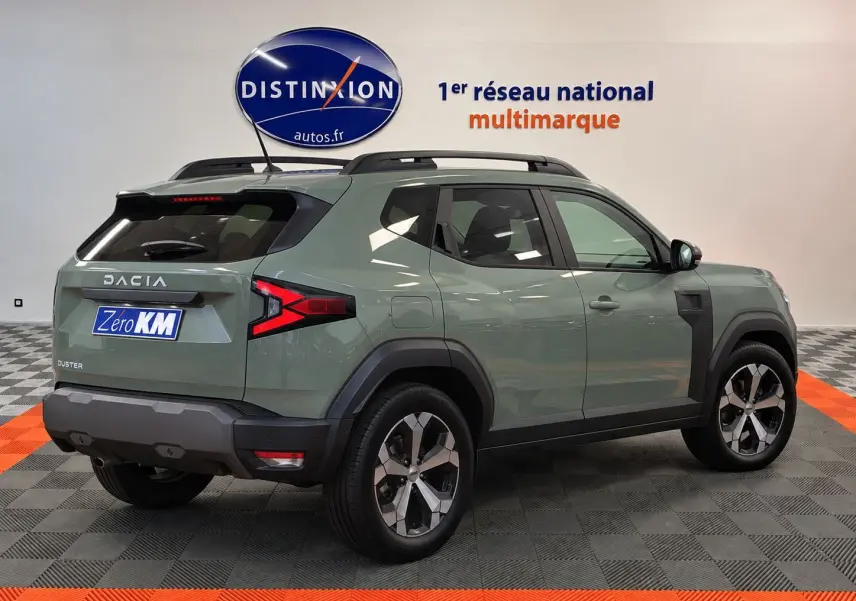 Vue 3/4 arrière droite du Dacia Duster 2026 vert cèdre avec jantes alliage et barres de toit noires.