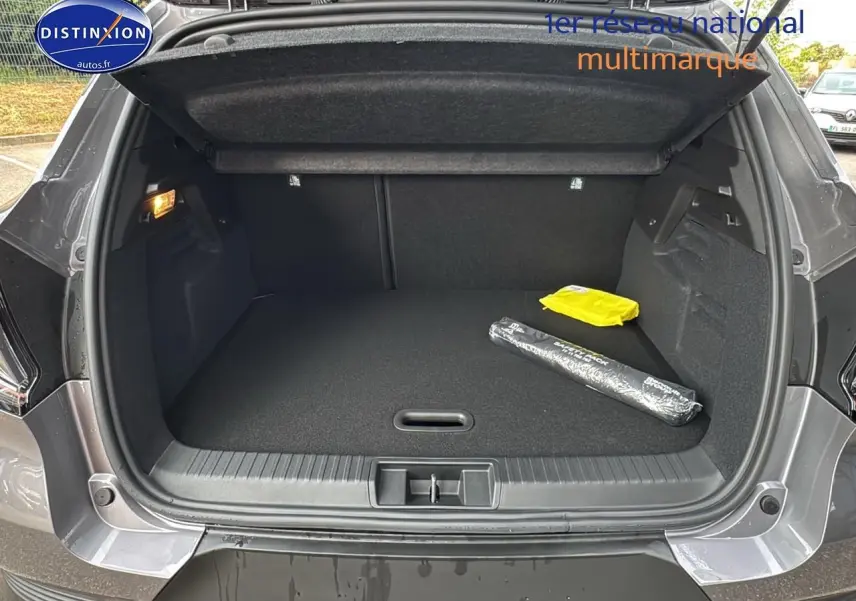 Coffre ouvert vu de l'arrière d'un Renault Captur gris cassiopée avec tapis noir et objets posés à droite