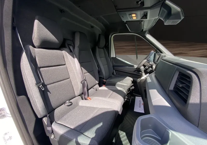 Intérieur du Renault Master 2025 vu côté passager, banquette tissu gris foncé avec rangements et tableau de bord gris.