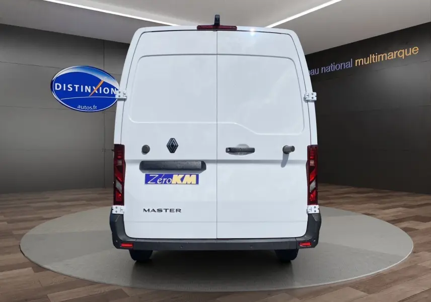 Vue arrière d’un utilitaire Renault Master blanc avec portes arrière tôlées et logo distinctif sur fond de showroom.