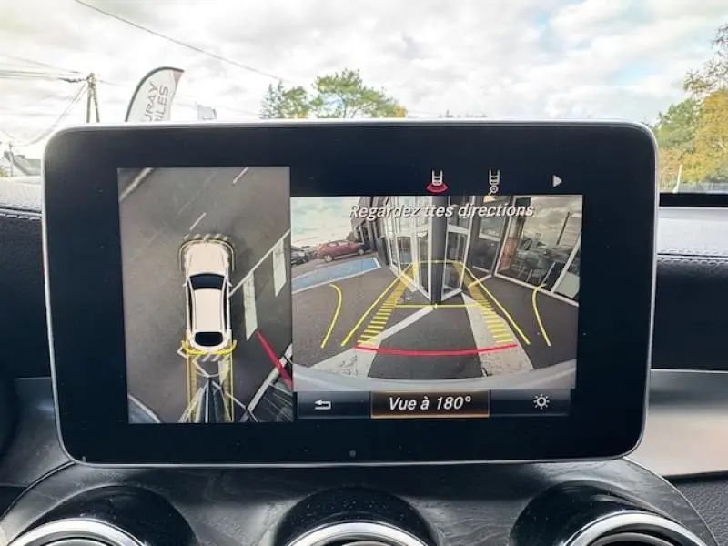 Écran multimédia montrant la caméra de recul et vue à 180° du Mercedes GLC Coupé blanc polaire en stationnement.