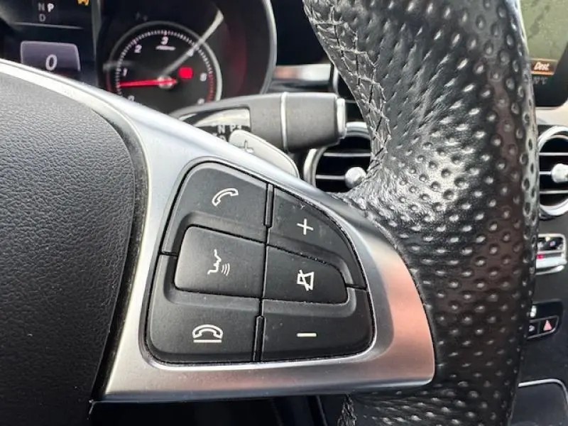 Gros plan sur les commandes du volant en cuir noir du Mercedes GLC Coupé blanc polaire, avec touches audio et téléphone.