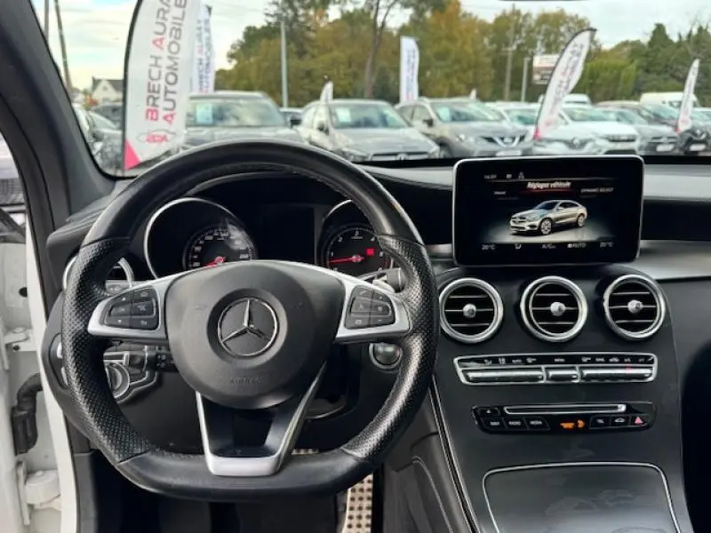 Vue intérieure du volant cuir noir et tableau de bord du Mercedes GLC Coupé blanc polaire avec écran multifonction allumé.