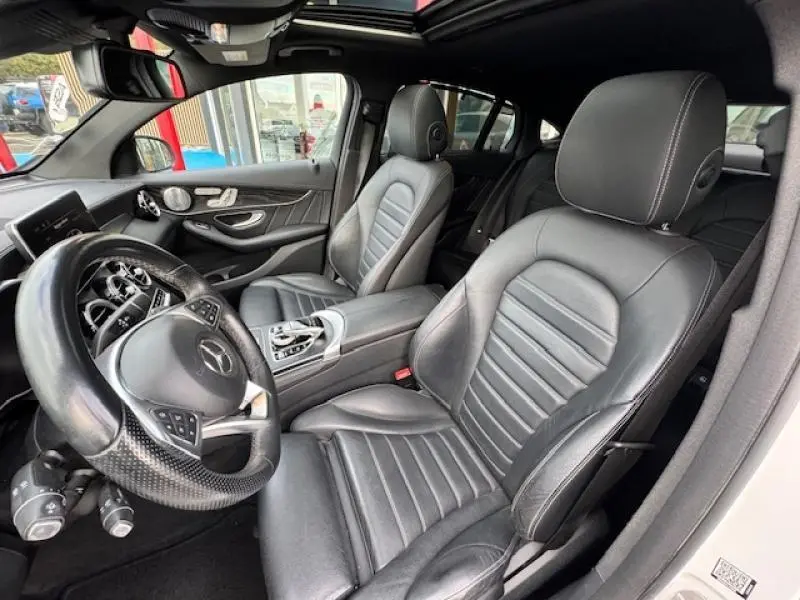 Vue intérieure avant du Mercedes GLC Coupé blanc polaire avec sièges sport cuir noir et toit ouvrant électrique.