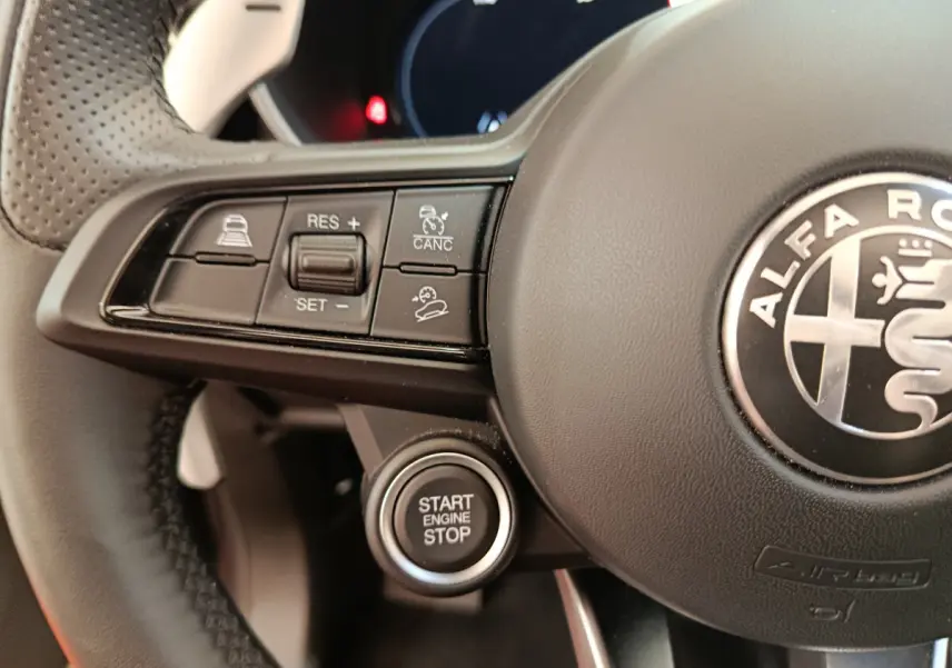 Gros plan sur le volant noir d'Alfa Romeo Stelvio avec boutons de régulateur et bouton démarrage Start Engine Stop.