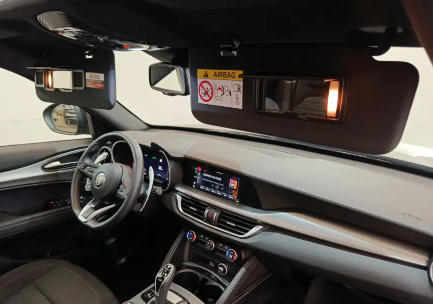 Intérieur de l'Alfa Romeo Stelvio 2024 vu côté conducteur, tableau de bord moderne avec écran tactile allumé.