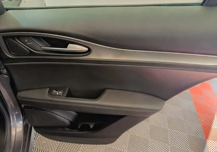 Vue intérieure côté gauche de la porte avant gris foncé de l'Alfa Romeo Stelvio 2024 avec poignée et commandes de vitre.