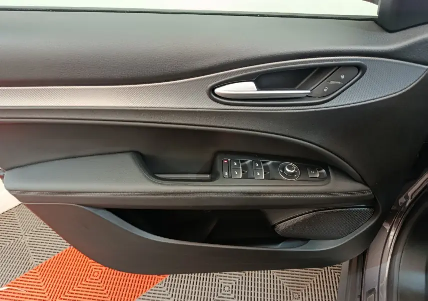 Vue rapprochée de la porte avant gauche de l'Alfa Romeo Stelvio gris foncé, avec commandes électriques et poignée argentée.