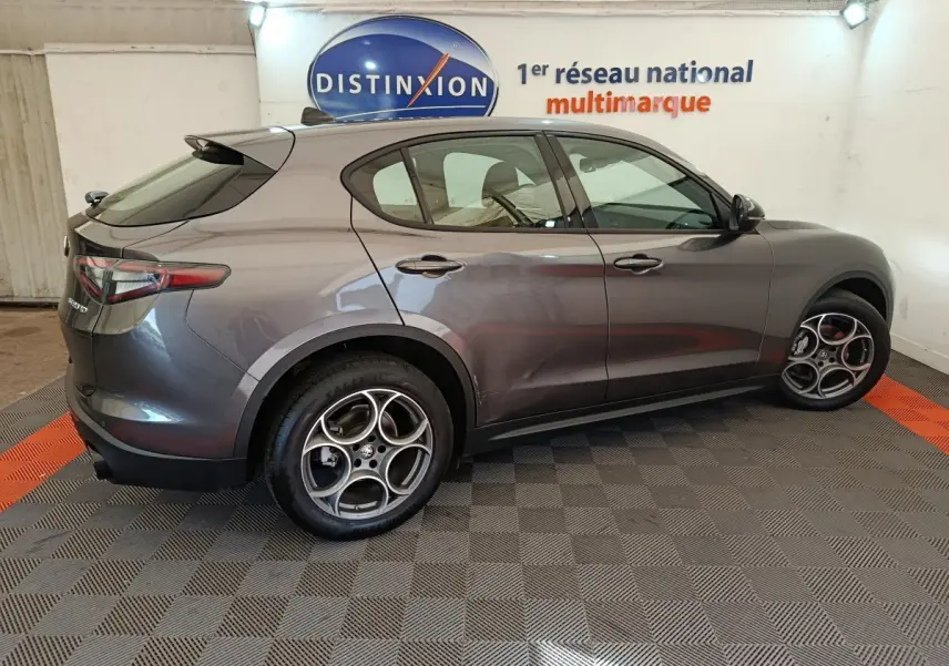 Vue de profil côté gauche d'un Alfa Romeo Stelvio gris foncé avec jantes distinctives en alliage, en intérieur showroom.