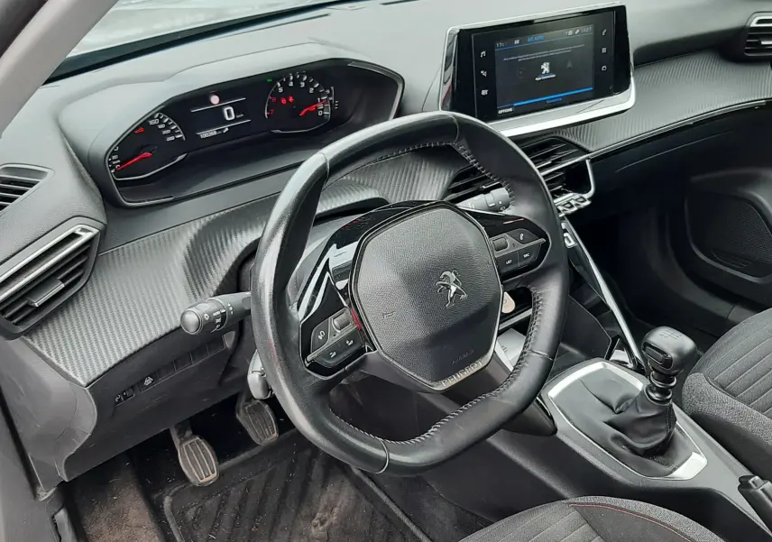 Vue intérieure côté conducteur du Peugeot 2008 gris, volant compact, tableau de bord numérique et levier de vitesses manuel.