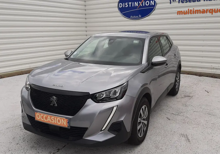 Peugeot 2008 gris Artense vue 3/4 avant droit, avec calandre noire et feux LED distinctifs, en extérieur sur parking.