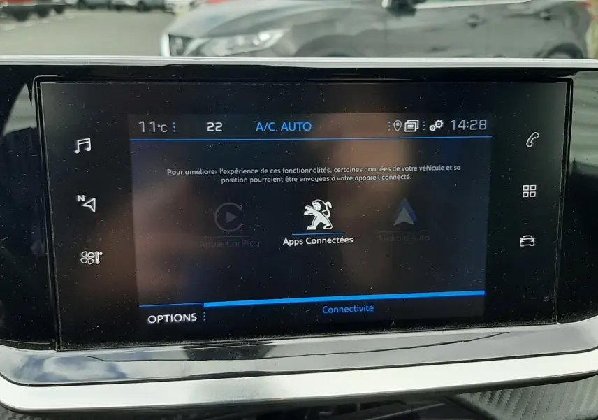 Vue de profil droit d’un Peugeot 2008 gris Artense garé en extérieur, avec une autre voiture floue en arrière-plan.