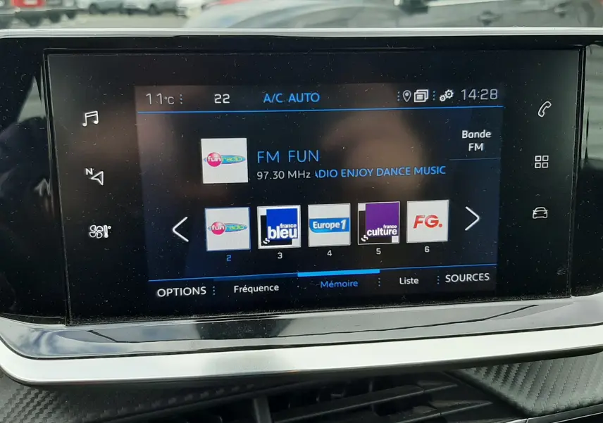 Vue intérieure sur l'écran tactile multimédia du Peugeot 2008 gris Artense, affichant les stations radio FM avec commandes tactiles.
