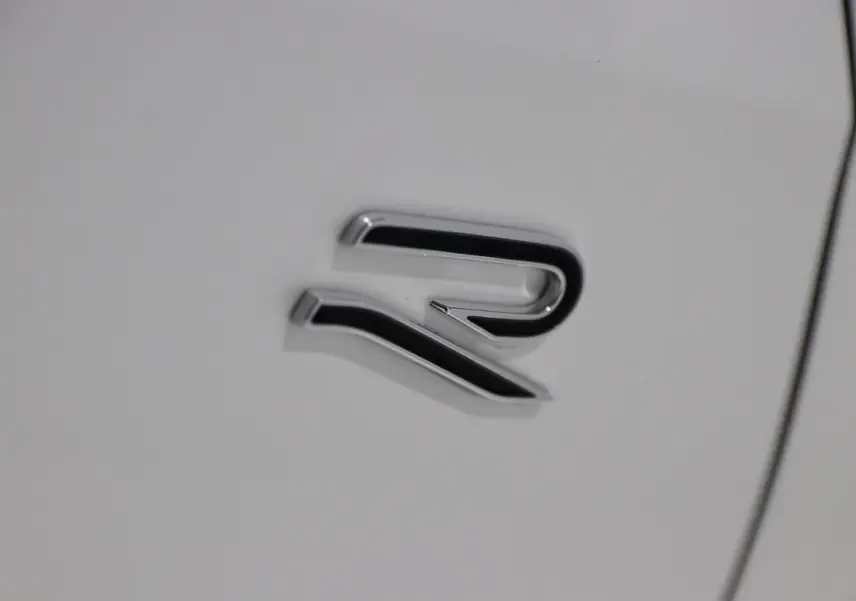 Gros plan sur l'emblème R chromé sur la carrosserie blanche d'une Volkswagen Golf 2.0 TDI 150 DSG R-Line.