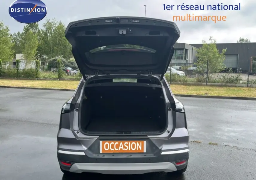 Vue arrière d'une Renault Symbioz gris cassiopée métal 2025 avec hayon ouvert montrant le coffre vide sur parking extérieur.