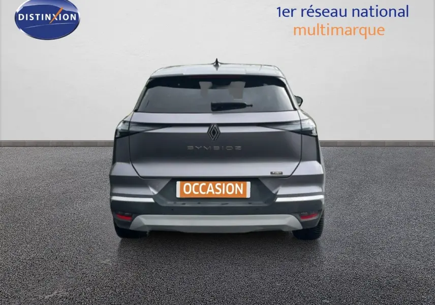 Vue arrière du Renault Symbioz gris cassiopée métal 2025 avec logo et feux LED distinctifs, en stationnement sur sol gris.