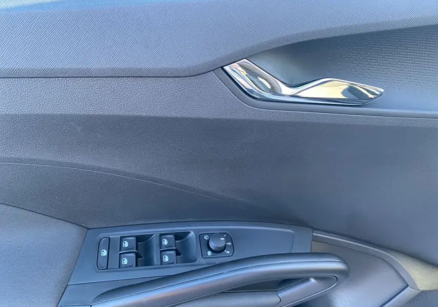 Détail de la porte côté gauche d'une Škoda Fabia 2024 gris/noir avec commandes des vitres et poignée chromée.