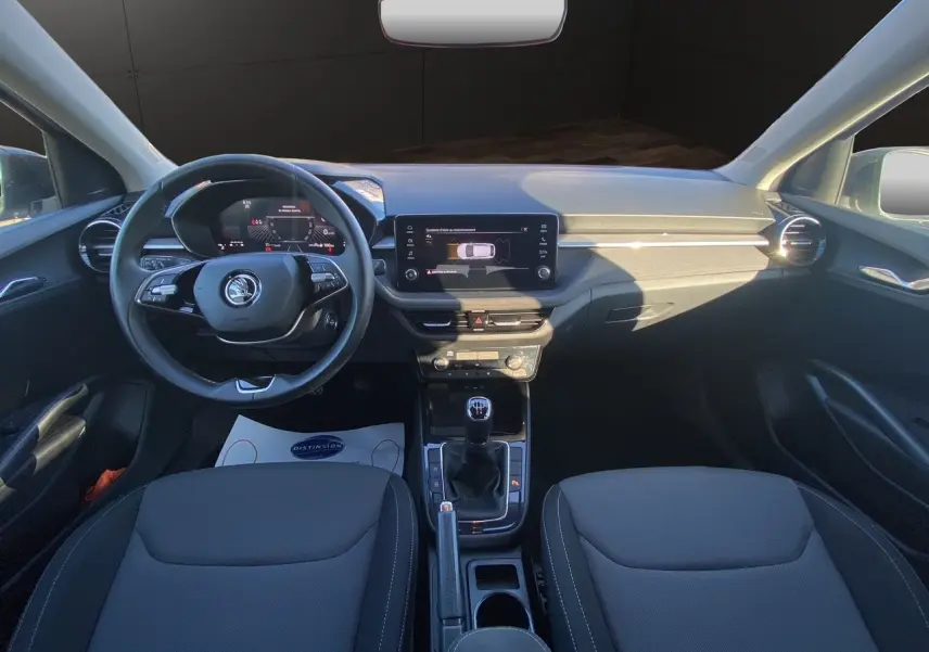 Intérieur avant de la Skoda Fabia 2024 gris/noir, vue frontale sur tableau de bord, volant cuir et écran tactile central.