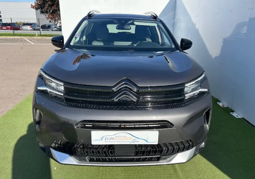 Citroën C5 Aircross gris platinium vue de face, avec calandre noire et barres de toit visibles sur fond extérieur.