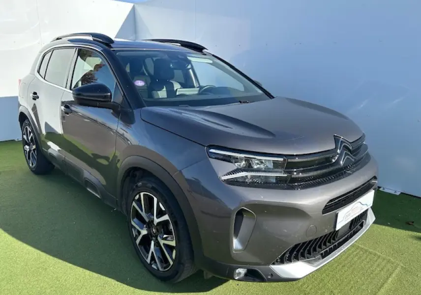 Citroën C5 Aircross gris platinium en 3/4 avant droit, avec barres de toit et jantes alliage noires.