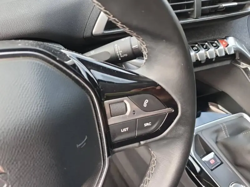 Gros plan sur le volant cuir noir à commandes audio et téléphone du Peugeot 3008 blanc nacré, avec console centrale visible en arrière-plan.