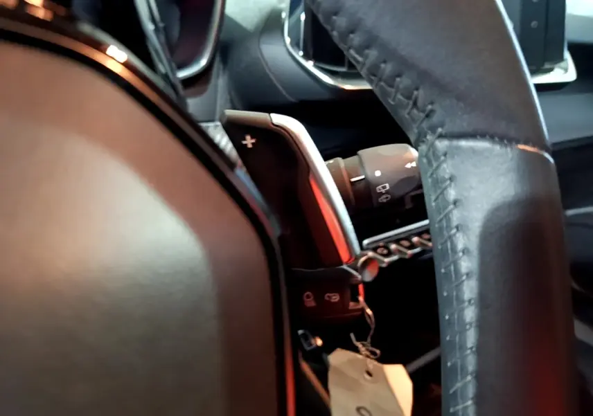 Gros plan sur le volant cuir noir et la palette de changement de vitesse à droite du Peugeot 2008 gris clair, intérieur moderne.