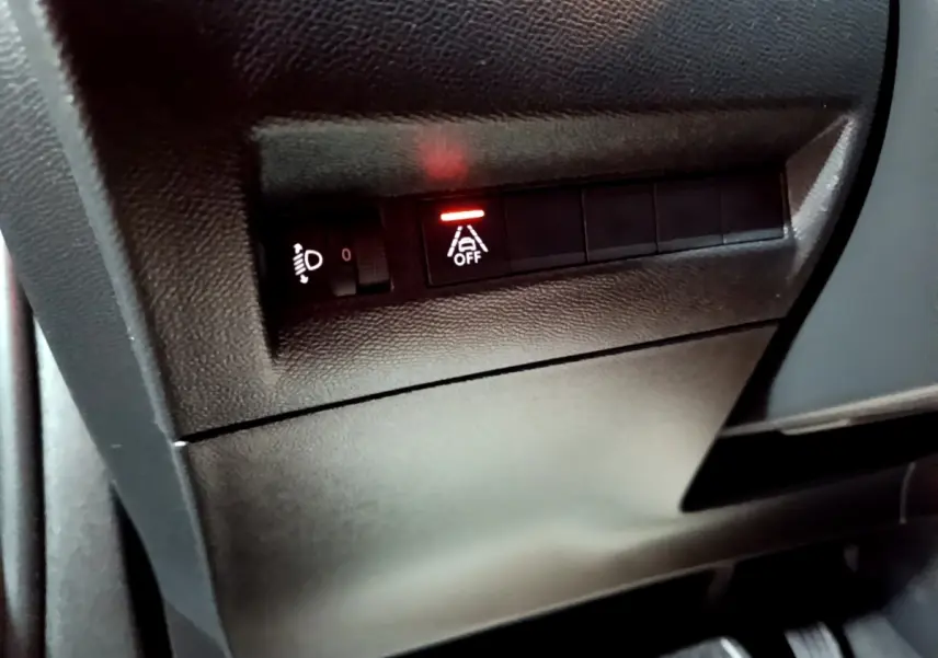 Gros plan sur les commandes noires du tableau de bord gauche du Peugeot 2008 gris clair, avec témoin d'alerte allumé.