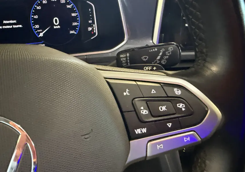 Gros plan sur le volant noir du Volkswagen T-Roc bleu 2022, avec commandes multifonctions et tableau de bord digital.