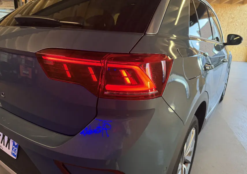 Vue arrière côté droit d’un Volkswagen T-Roc bleu avec feux arrière allumés dans un garage.