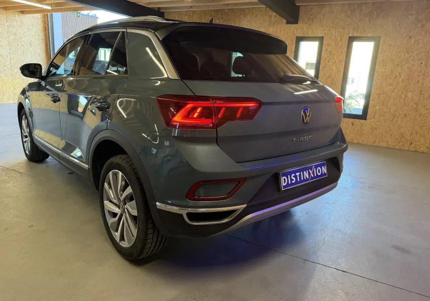 Vue 3/4 arrière droite d'un Volkswagen T-Roc bleu 2022 avec feux arrière allumés dans un garage.