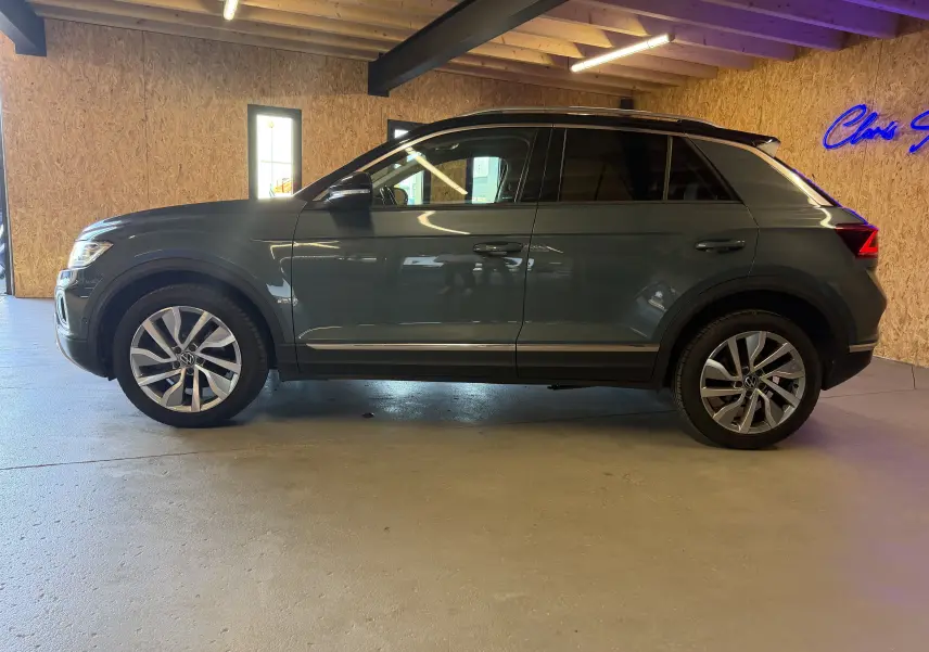 Vue de profil côté gauche d'un Volkswagen T-Roc bleu 2022, avec jantes alliage et toit noir en intérieur lumineux.