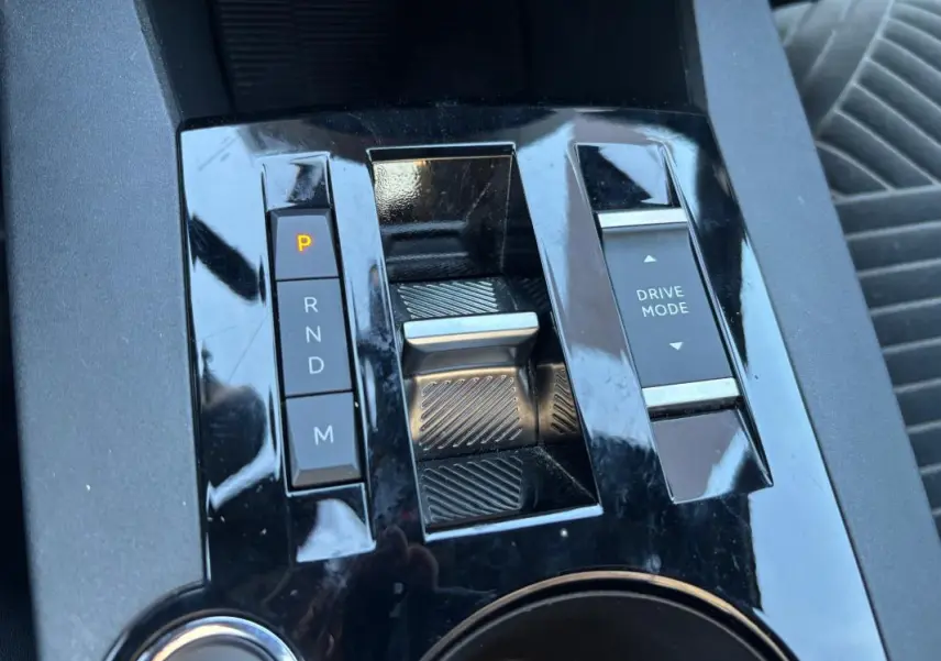 Gros plan sur la console centrale noire brillante de la Lancia Ypsilon 2025, montrant la sélection de boîte auto et le bouton Drive Mode.