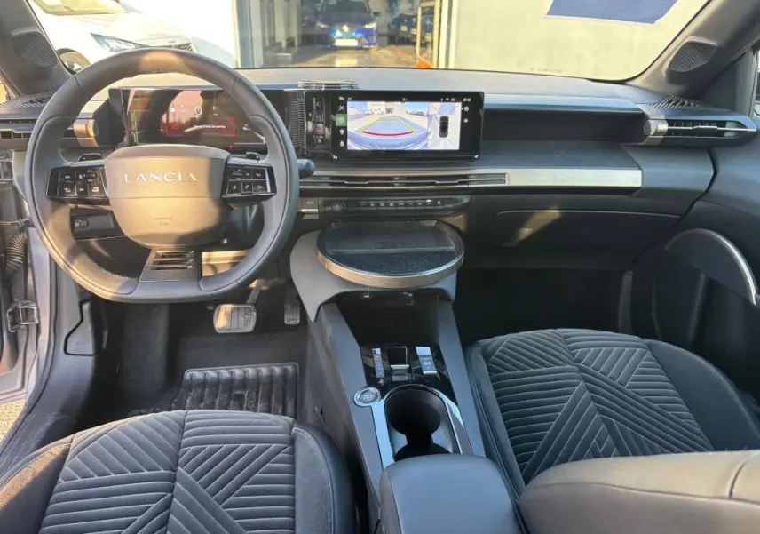 Vue intérieure avant de la Lancia Ypsilon gris 2025, montrant le tableau de bord avec écran central et volant sport multifonction.