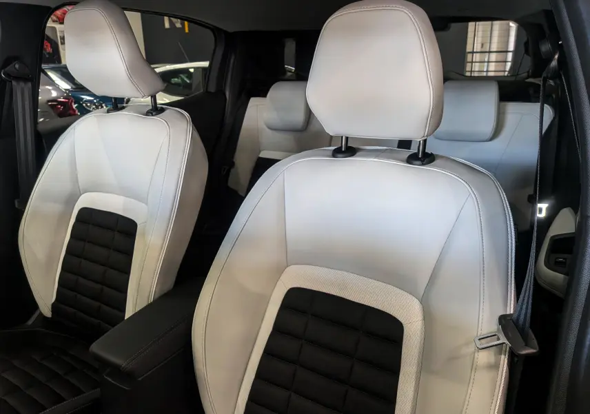 Gros plan sur les sièges avant en cuir bi-ton blanc et noir du Citroën C3 Aircross hybride 2026, intérieur spacieux.