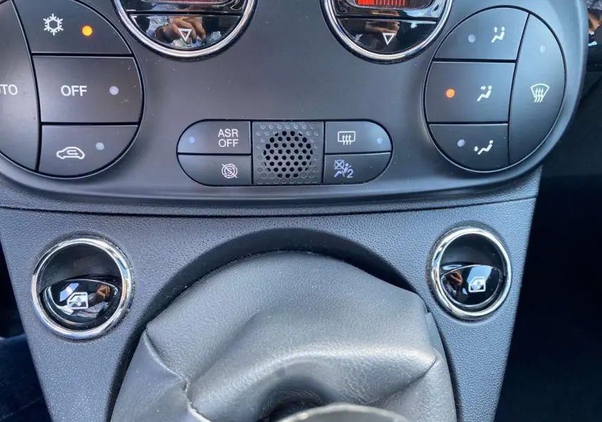 Gros plan sur la console centrale de la Fiat 500 noire 2024, montrant les commandes de climatisation et les boutons des vitres électriques.