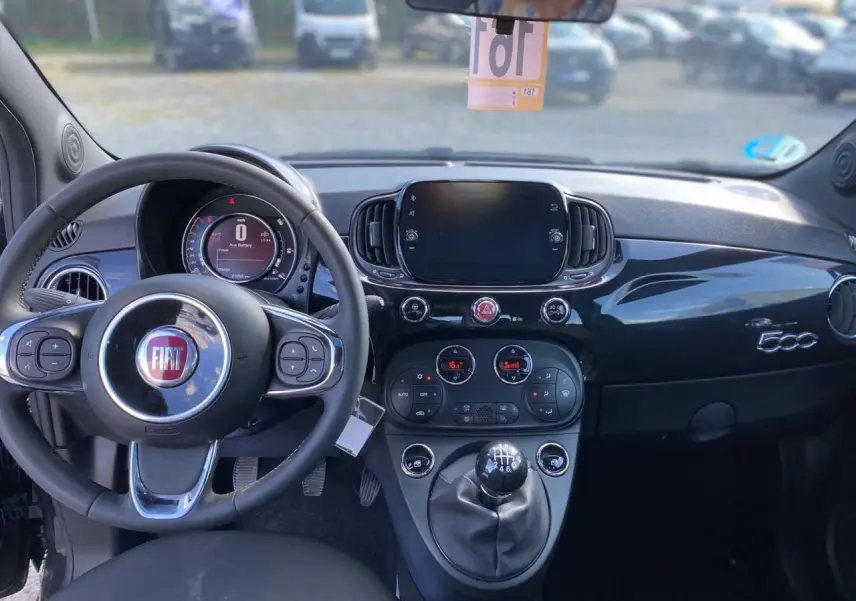 Vue intérieure du tableau de bord noir brillant de la Fiat 500 2024 avec volant multifonction et levier de vitesse manuel.