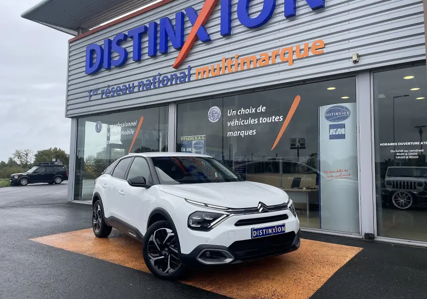 Citroën C4 blanc en 3/4 avant droit, avec jantes noires et toit noir, devant une concession Distinxion.