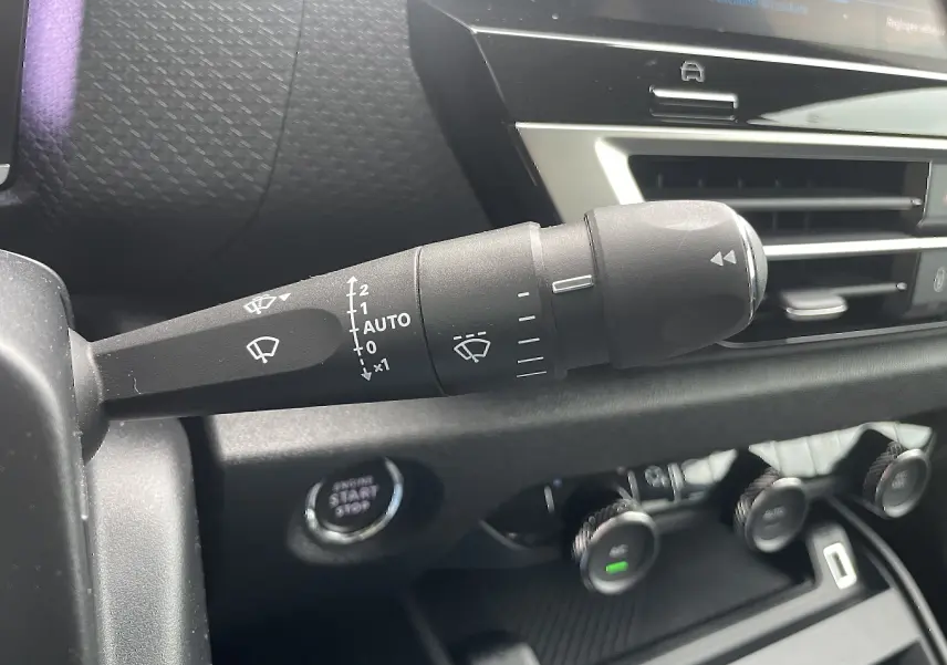 Gros plan sur la commande d'essuie-glace à gauche du volant dans l'habitacle noir d'une Citroën C4 blanche 2022.