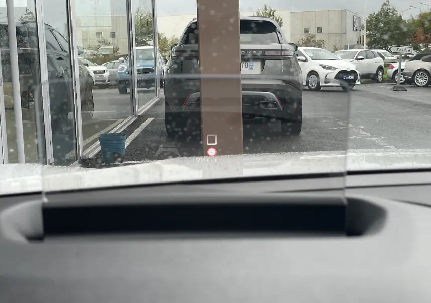 Vue depuis l'habitacle d'une Citroën C4 blanche, avec un SUV gris en arrière-plan et un panneau "Sortie" visible.