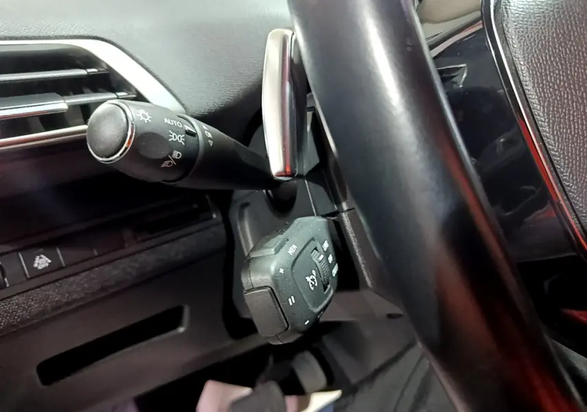 Gros plan sur la commande multifonctions et la manette des phares derrière le volant cuir noir du Peugeot 3008 2022.