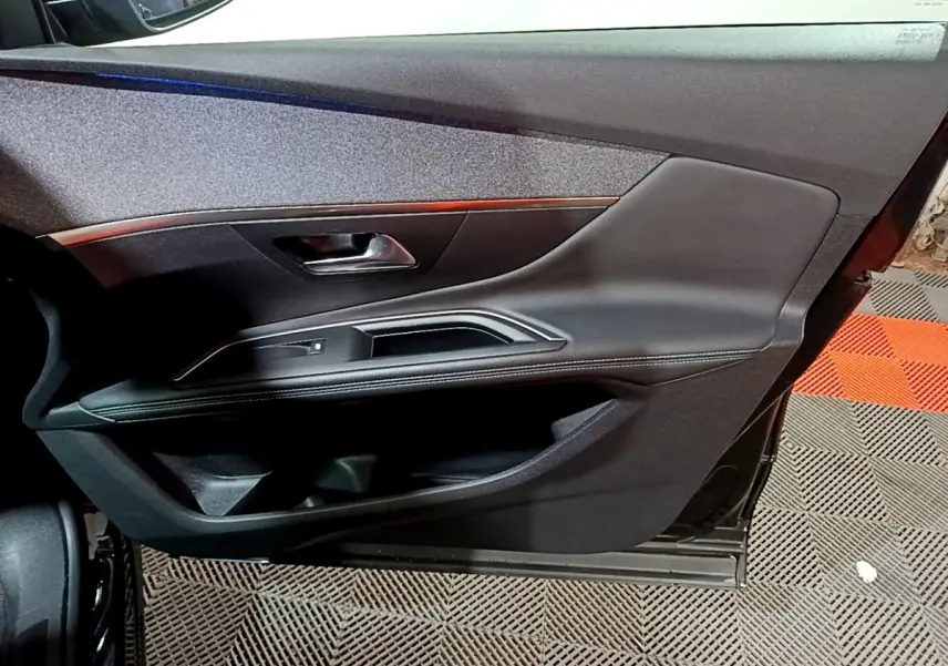 Gros plan sur la porte intérieure côté conducteur noire du Peugeot 3008 2022 avec poignée métallique et surpiqûres blanches.