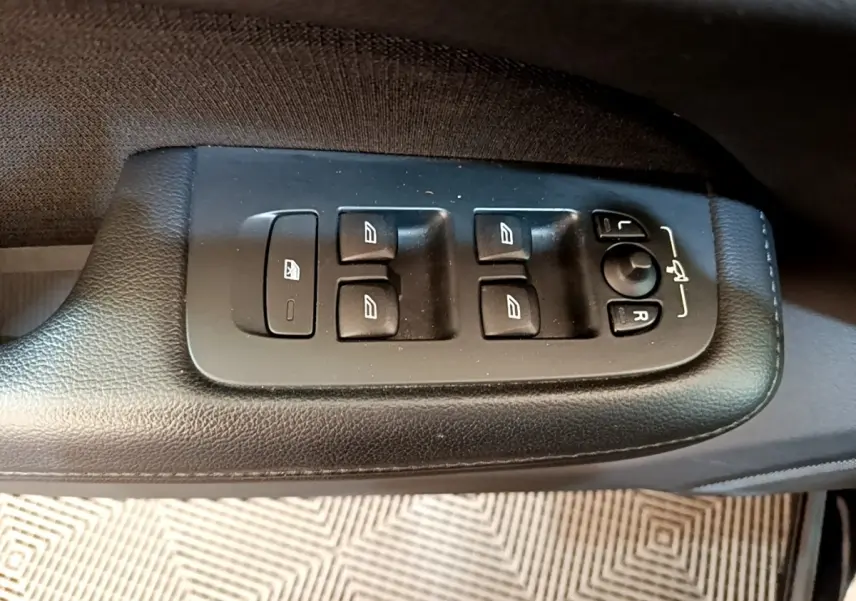 Gros plan sur les commandes de lève-vitres et réglage des rétroviseurs côté conducteur d'une Volvo V60 noire de 2020.