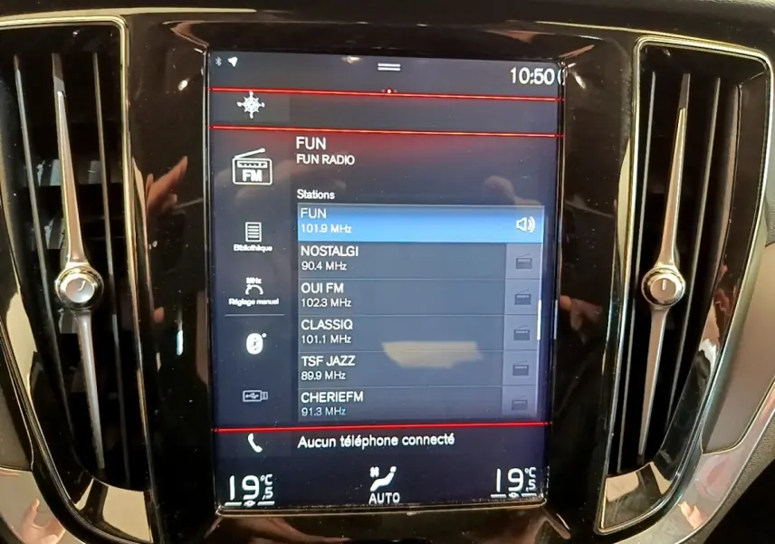 Écran tactile central de la Volvo V60 noir, affichant les stations radio avec ventilation et réglages climatisation visibles.