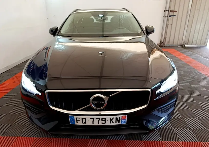 Vue avant d'une Volvo V60 noire 2020 avec phares LED allumés dans un garage au sol damier noir et rouge.